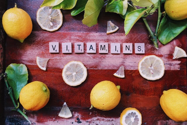 The word vitamins spelled out with scrabble tiles surrounded by lemons.